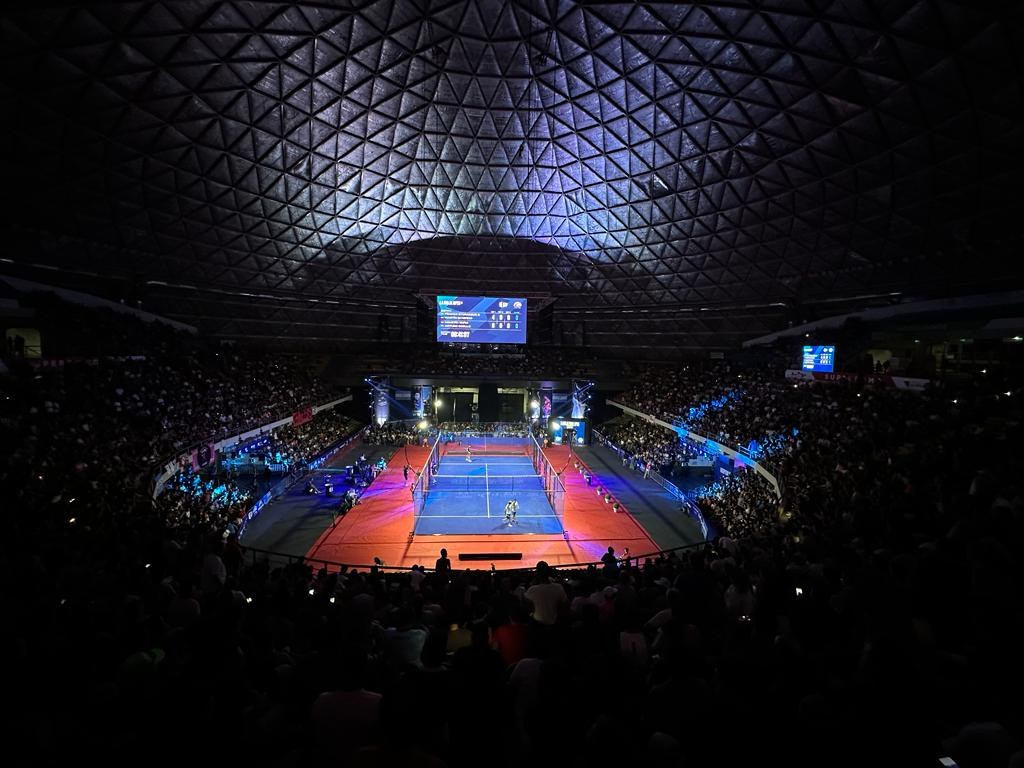 Estadio de pádel colmado con iluminación dorada durante un partido